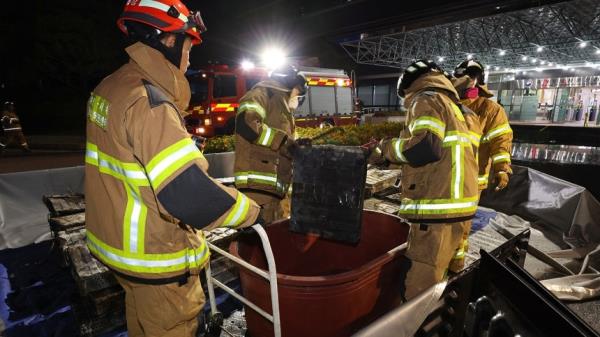 Firefighters move burnt lithium-ion batteries at the scene of the fire at the National Information Resources Service in Daejeon on Friday night. (Yonhap)