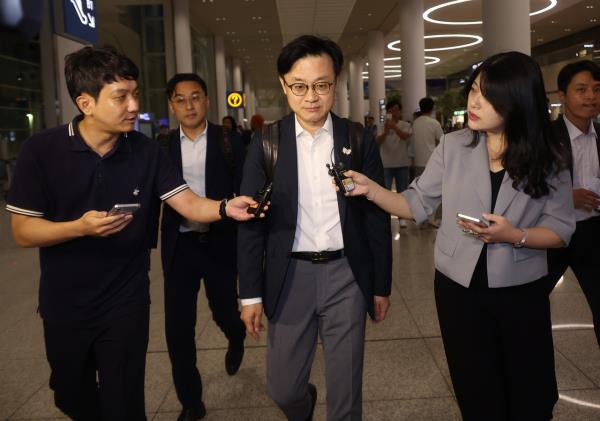 Industry Minister Kim Jung-kwan (center) is questioned by reporters upon arrival at Incheon Airport on Sunday. (Yonhap)